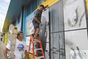 Eugene Price, left, owner of PD Technologies, and employee Darren DeMello install vinyl artwork on the side of a building in Kakaako.